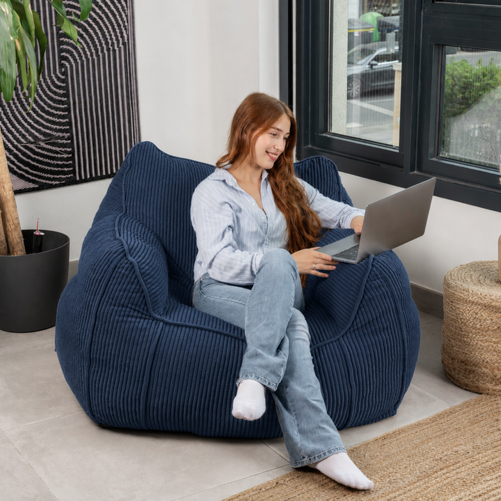 Personne assise sur le pouf fauteuil en velours côtelé bleu foncé, dans un salon