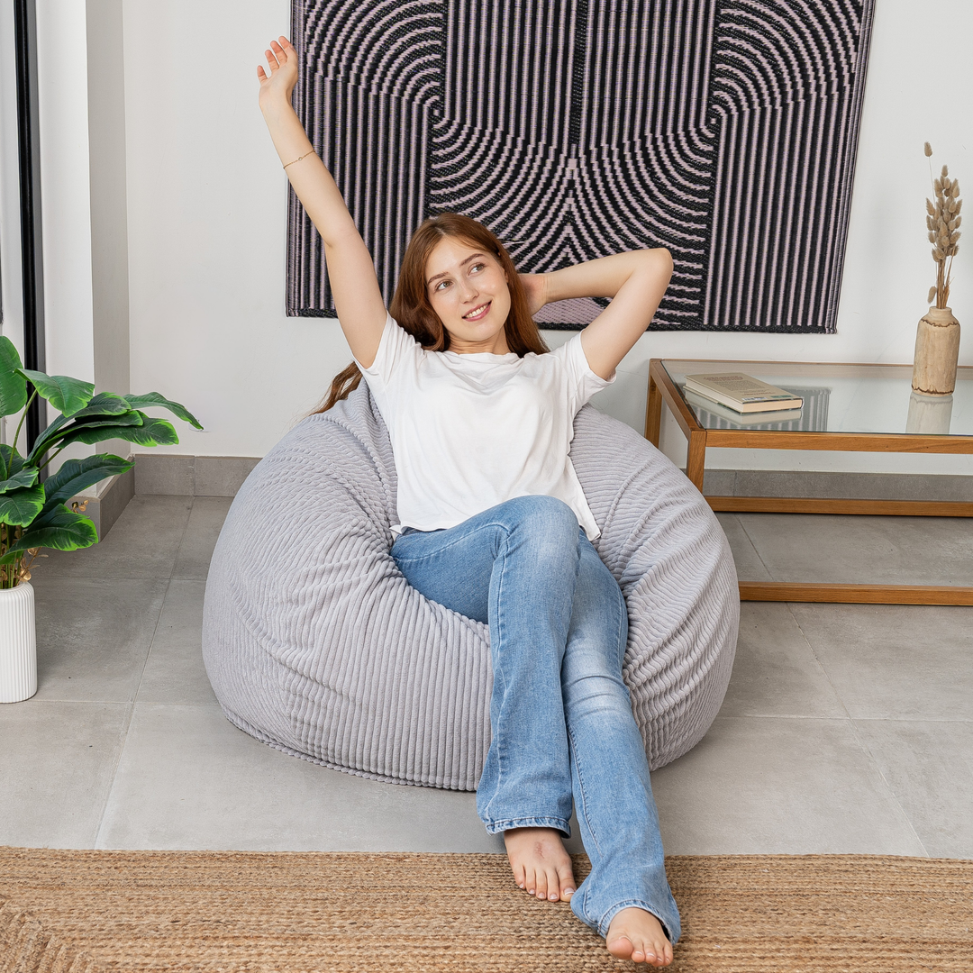 Femme assise sur un pouf poire déhoussable en velours côtelé, dans un salon
