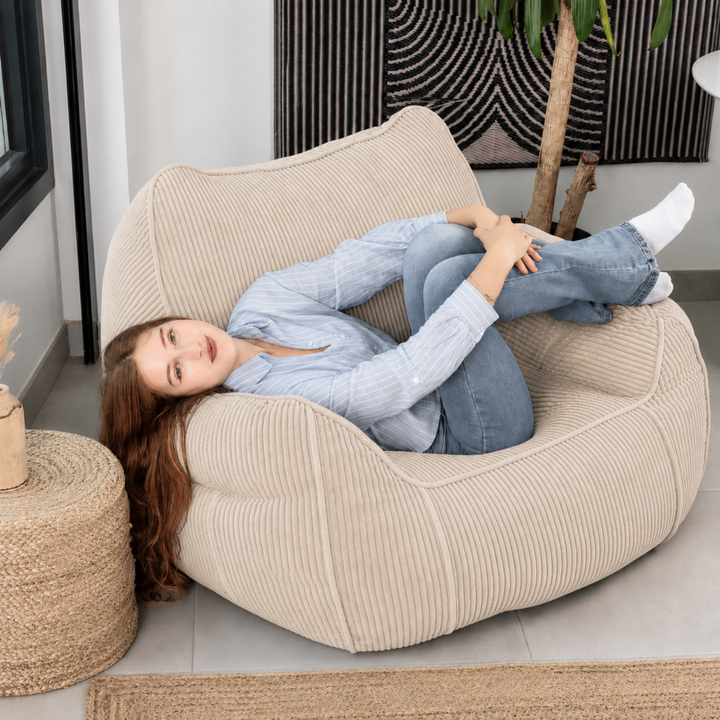 Personne assise sur le pouf fauteuil en velours côtelé beige, dans un salon