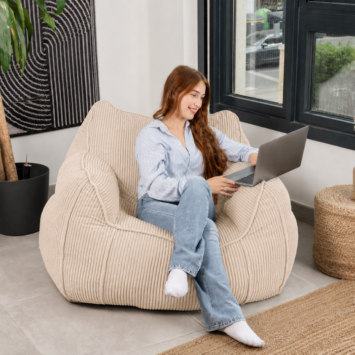 Personne assise sur le pouf fauteuil en velours côtelé beige, dans un salon