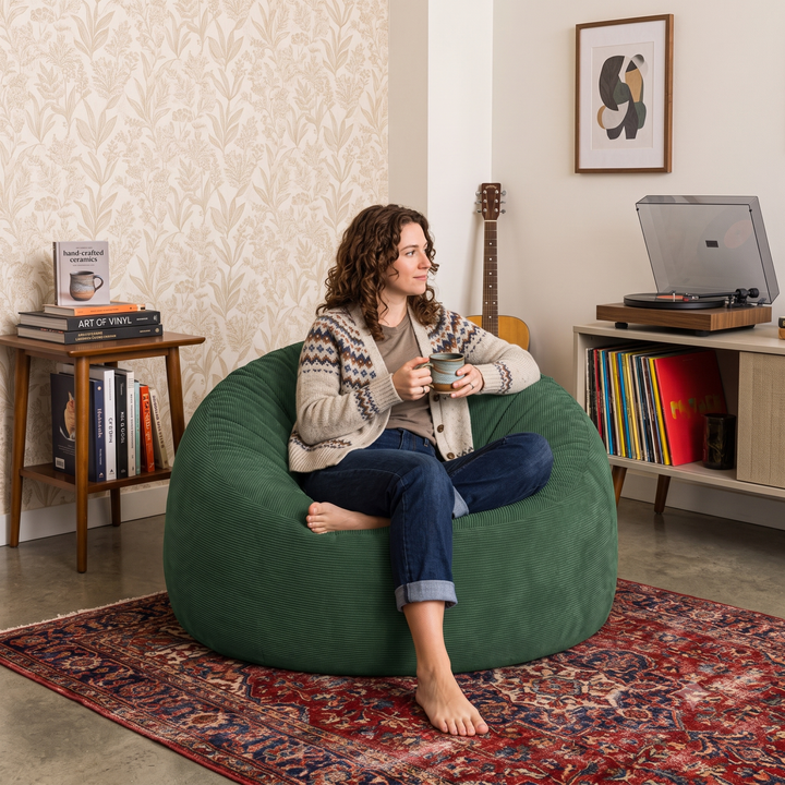 Femme assise sur un pouf déhoussable 100 cm en velours côtelé vert foncé, forme ronde pour s’asseoir.