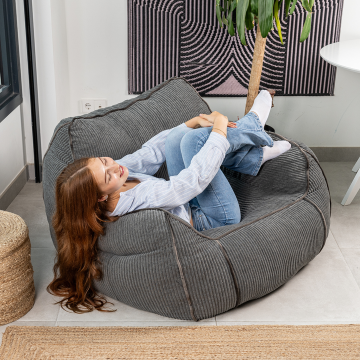 Personne assise sur le pouf fauteuil en velours côtelé gris foncé, dans un salon